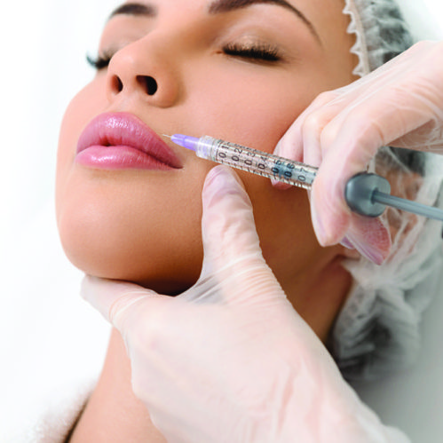 Close up of surgeon arms making botox injection into female face. Serene young woman is lying and relaxing